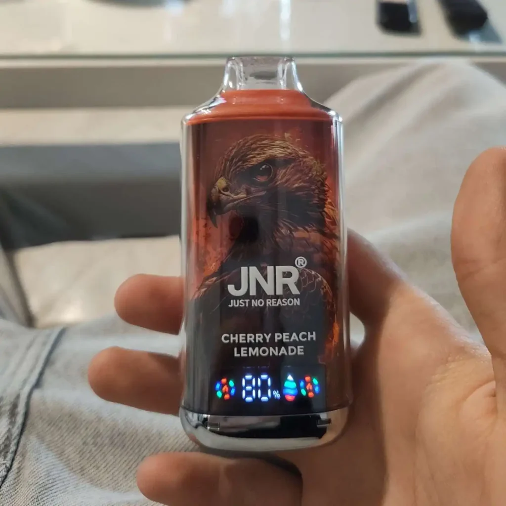 Puff JNR Falcon X Cherry Peach Lemonade tenue en main, écran LED affichant 80 %
